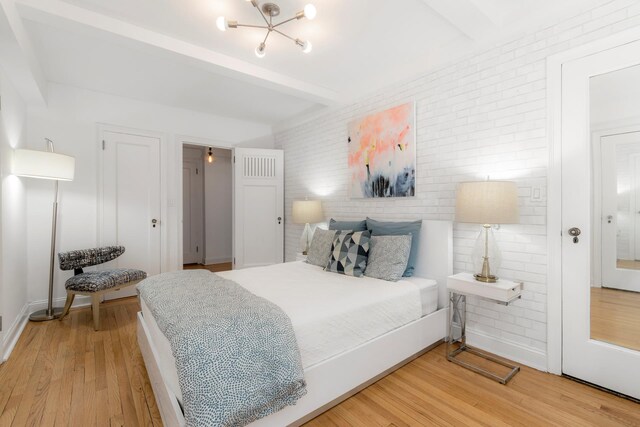 bedroom with light wood-style floors, beam ceiling, and brick wall