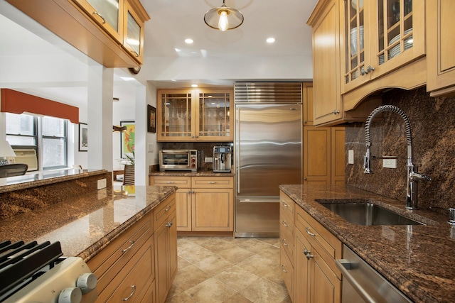 kitchen with stainless steel appliances, glass insert cabinets, a sink, and tasteful backsplash