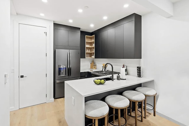 kitchen with a breakfast bar area, a sink, light wood-style floors, dark cabinetry, and stainless steel fridge