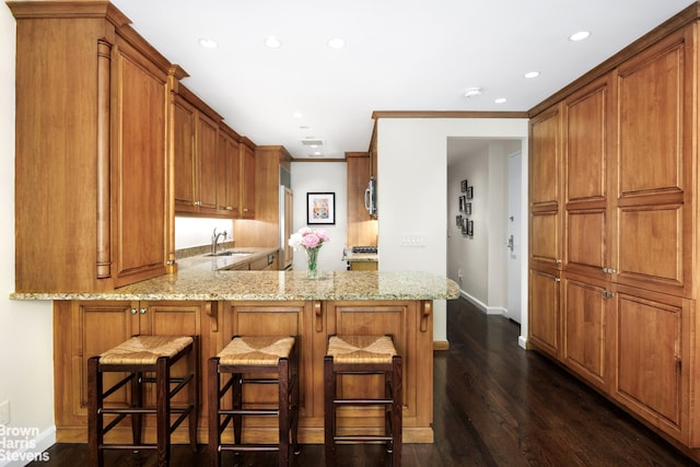 kitchen featuring light stone counters, brown cabinetry, and a sink