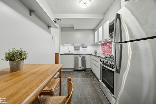 kitchen featuring white cabinets, dark tile patterned flooring, stainless steel appliances, a textured ceiling, and a sink