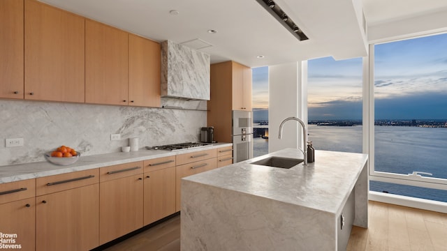 kitchen with wall chimney exhaust hood, light brown cabinetry, and a sink