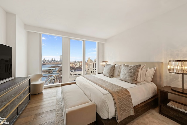 bedroom with expansive windows, wood-type flooring, and a city view