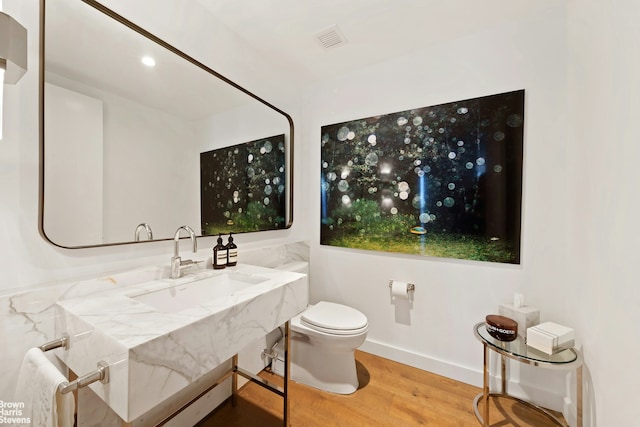 half bathroom with toilet, a sink, visible vents, wood finished floors, and baseboards