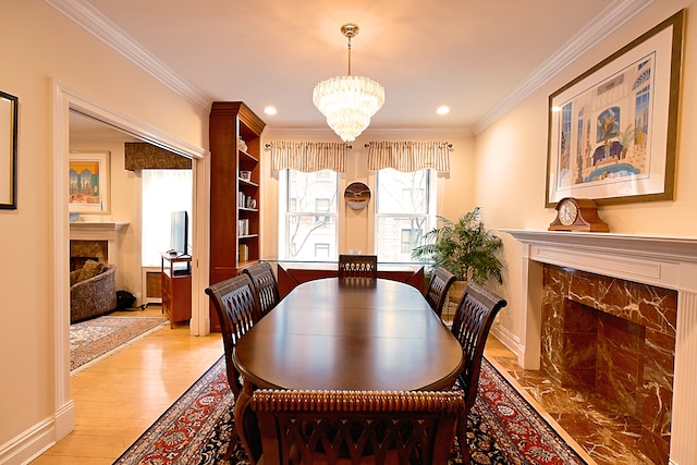 dining room featuring light wood-style flooring, a notable chandelier, recessed lighting, a high end fireplace, and crown molding