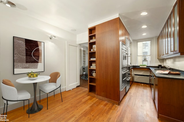 kitchen featuring dark countertops, light wood-type flooring, a sink, open shelves, and baseboards