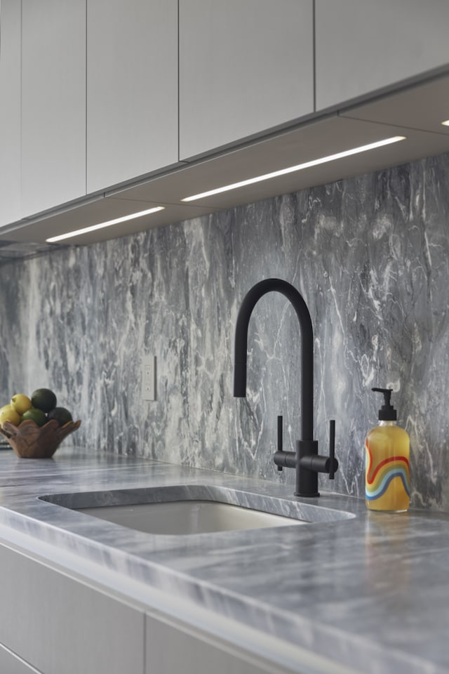 room details with stainless steel counters, white cabinetry, decorative backsplash, and a sink