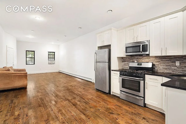 kitchen with a baseboard heating unit, tasteful backsplash, dark countertops, dark wood-style floors, and appliances with stainless steel finishes