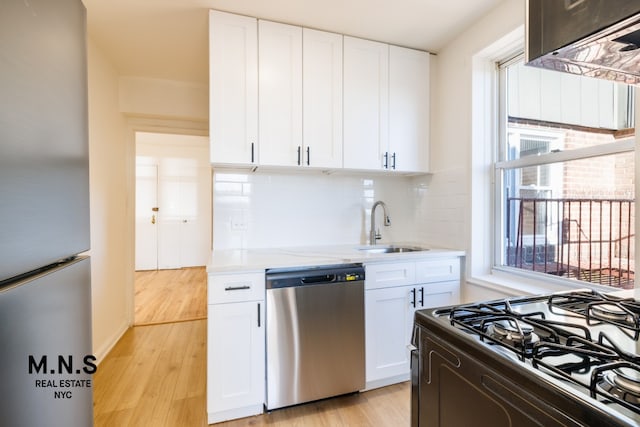 kitchen featuring light wood-style flooring, a sink, white cabinets, appliances with stainless steel finishes, and decorative backsplash