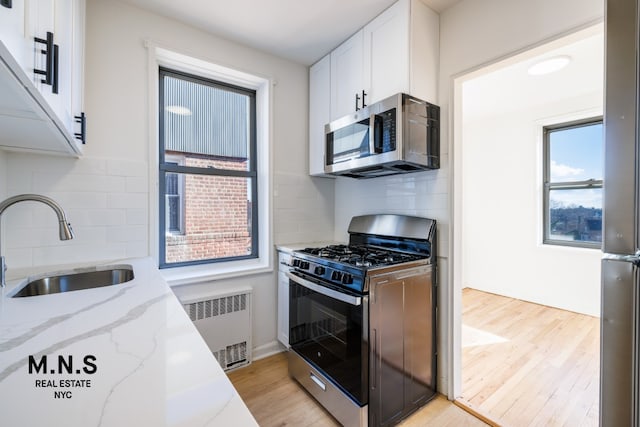 kitchen featuring stainless steel appliances, a sink, light wood finished floors, and radiator heating unit