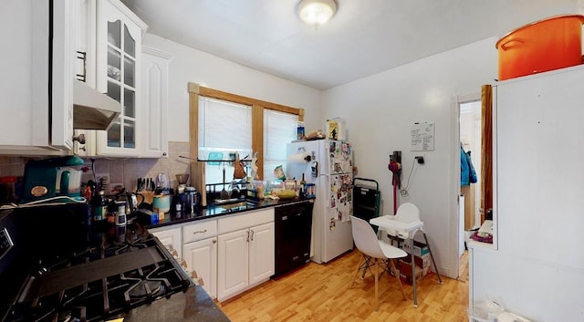 kitchen featuring dark countertops, dishwasher, light wood-style flooring, freestanding refrigerator, and a sink