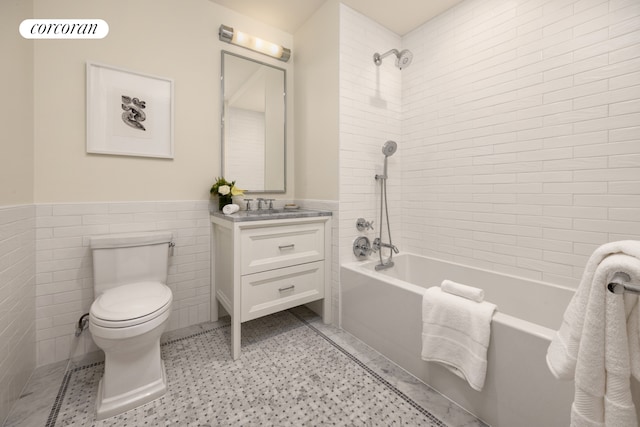 full bath featuring tile walls, toilet, washtub / shower combination, wainscoting, and vanity