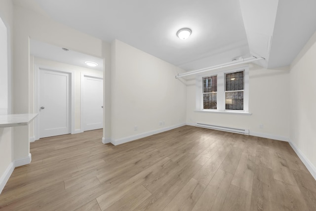 empty room featuring baseboards, a baseboard radiator, and light wood-style floors