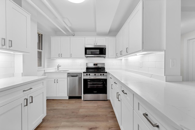 kitchen featuring light wood finished floors, a sink, stainless steel appliances, white cabinetry, and backsplash