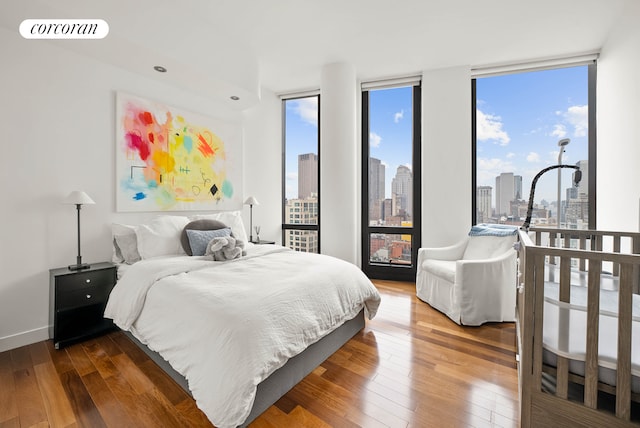 bedroom with baseboards, floor to ceiling windows, a view of city, and wood-type flooring