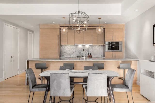 kitchen featuring light wood-style flooring, stainless steel oven, decorative backsplash, modern cabinets, and an inviting chandelier