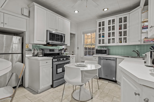 kitchen with decorative backsplash, white cabinetry, stainless steel appliances, light countertops, and glass insert cabinets