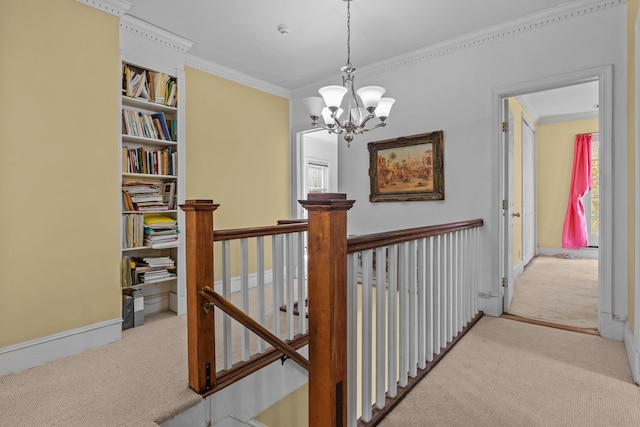 hall with baseboards, ornamental molding, an upstairs landing, carpet floors, and an inviting chandelier