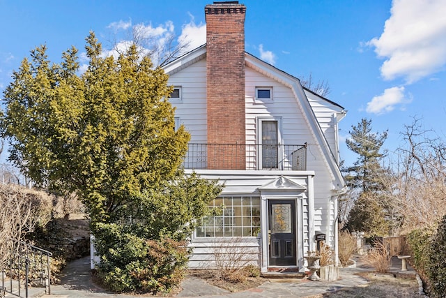 view of front of house with a balcony, a gambrel roof, and a chimney