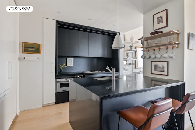 kitchen with light wood-style flooring, a sink, oven, a kitchen bar, and dark cabinets