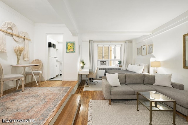 bedroom with freestanding refrigerator, radiator heating unit, wood finished floors, and beam ceiling