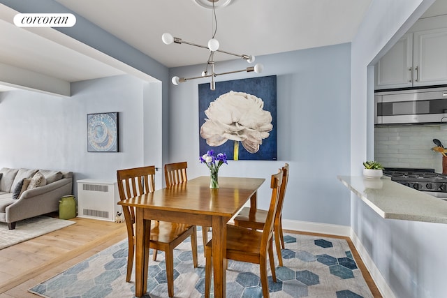 dining space with radiator heating unit, light wood-style floors, visible vents, and baseboards