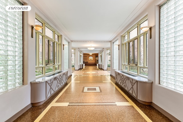 corridor featuring light speckled floor, baseboards, a wealth of natural light, and ornamental molding