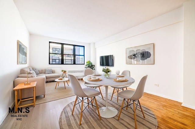 dining space with radiator heating unit, baseboards, and light wood-style flooring