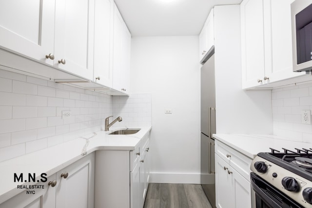 kitchen featuring stainless steel appliances, dark wood-style flooring, a sink, white cabinets, and light stone countertops