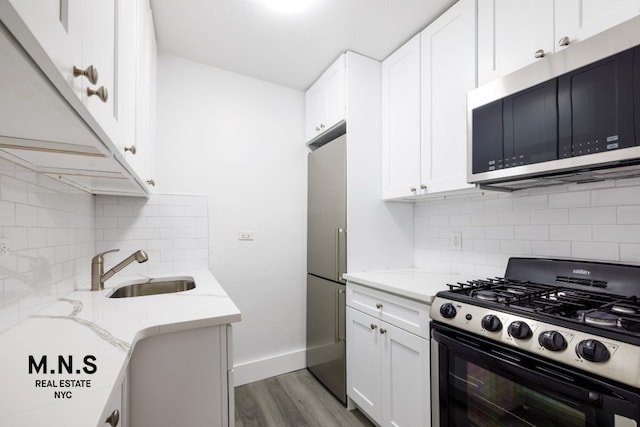 kitchen with light stone counters, appliances with stainless steel finishes, white cabinetry, a sink, and wood finished floors