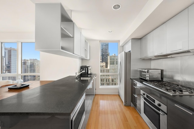 kitchen featuring a city view, dark countertops, appliances with stainless steel finishes, white cabinetry, and light wood-type flooring