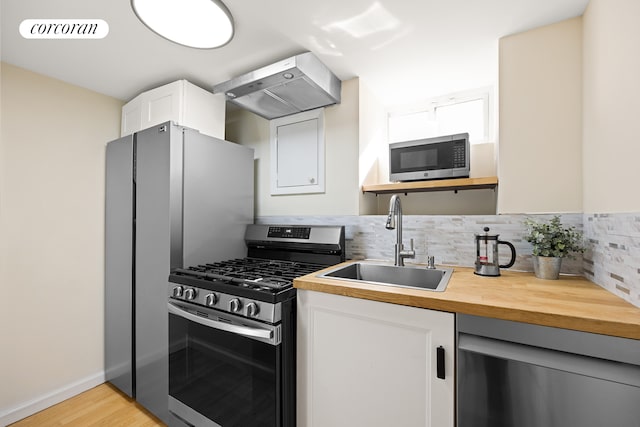 kitchen featuring visible vents, stainless steel appliances, wall chimney range hood, wooden counters, and a sink