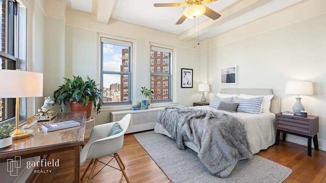 bedroom with radiator, baseboards, beam ceiling, and wood finished floors