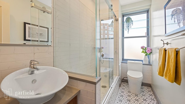 full bath featuring toilet, a stall shower, tile walls, and a sink