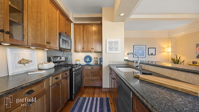 kitchen with appliances with stainless steel finishes, dark wood-style flooring, a sink, and dark stone countertops