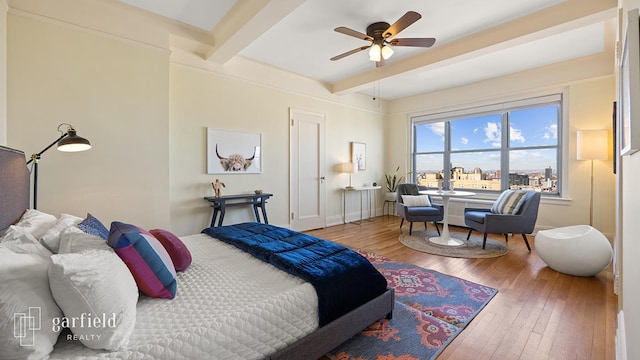 bedroom featuring hardwood / wood-style flooring, a ceiling fan, baseboards, and beam ceiling