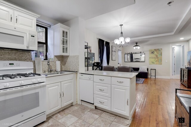 kitchen featuring backsplash, open floor plan, a sink, white appliances, and a peninsula