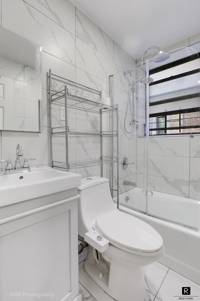 bathroom with marble finish floor, shower / bath combination with glass door, tile walls, toilet, and vanity