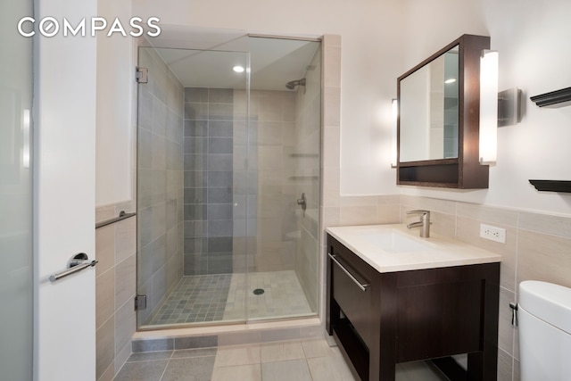 full bath with a shower stall, tile walls, toilet, tile patterned flooring, and vanity