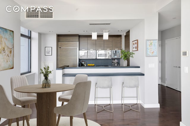 kitchen featuring stainless steel microwave, dark wood-type flooring, decorative backsplash, hanging light fixtures, and baseboards