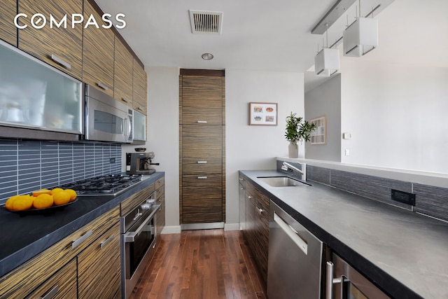 kitchen with stainless steel appliances, dark countertops, tasteful backsplash, a sink, and dark wood-type flooring