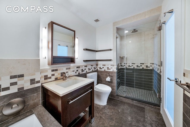 bathroom with tile walls, a shower stall, vanity, toilet, and a wainscoted wall