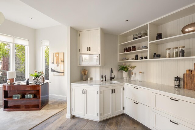 kitchen featuring open shelves, a sink, wood finished floors, white cabinets, and white microwave