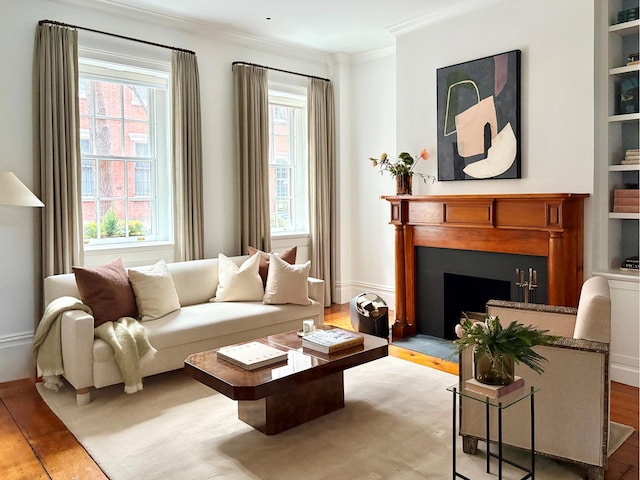 sitting room with baseboards, built in features, ornamental molding, a fireplace, and wood finished floors