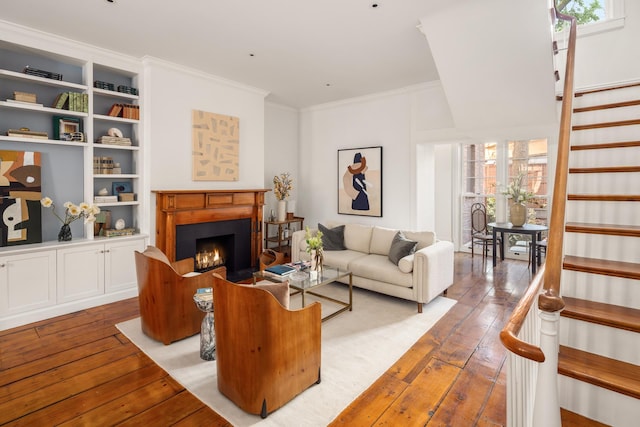 living room featuring a warm lit fireplace, ornamental molding, stairs, and light wood finished floors