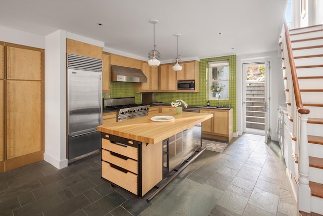 kitchen with butcher block countertops, a sink, wall chimney exhaust hood, decorative backsplash, and built in appliances