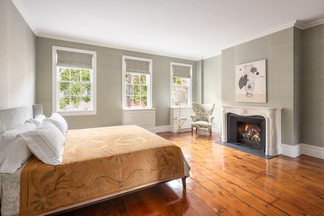 bedroom featuring baseboards, a lit fireplace, hardwood / wood-style floors, and crown molding