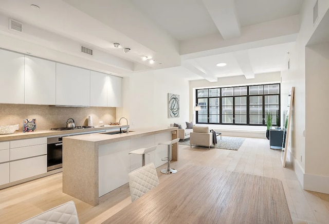 kitchen with modern cabinets, beamed ceiling, a sink, and oven