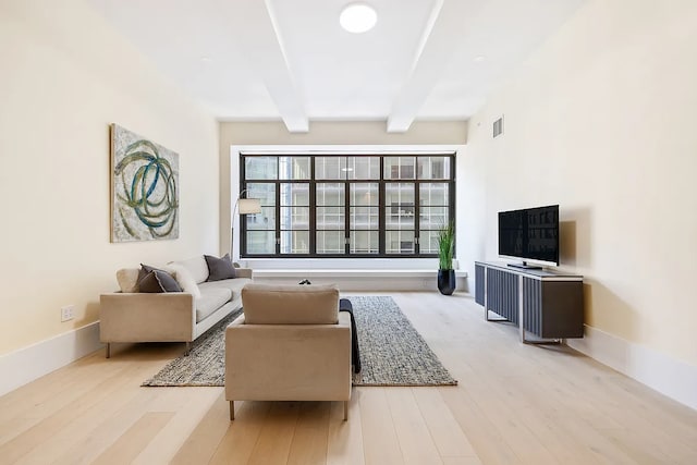 living room featuring visible vents, light wood finished floors, beam ceiling, and baseboards