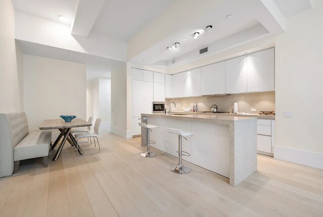 living room featuring visible vents, light wood finished floors, beam ceiling, and baseboards